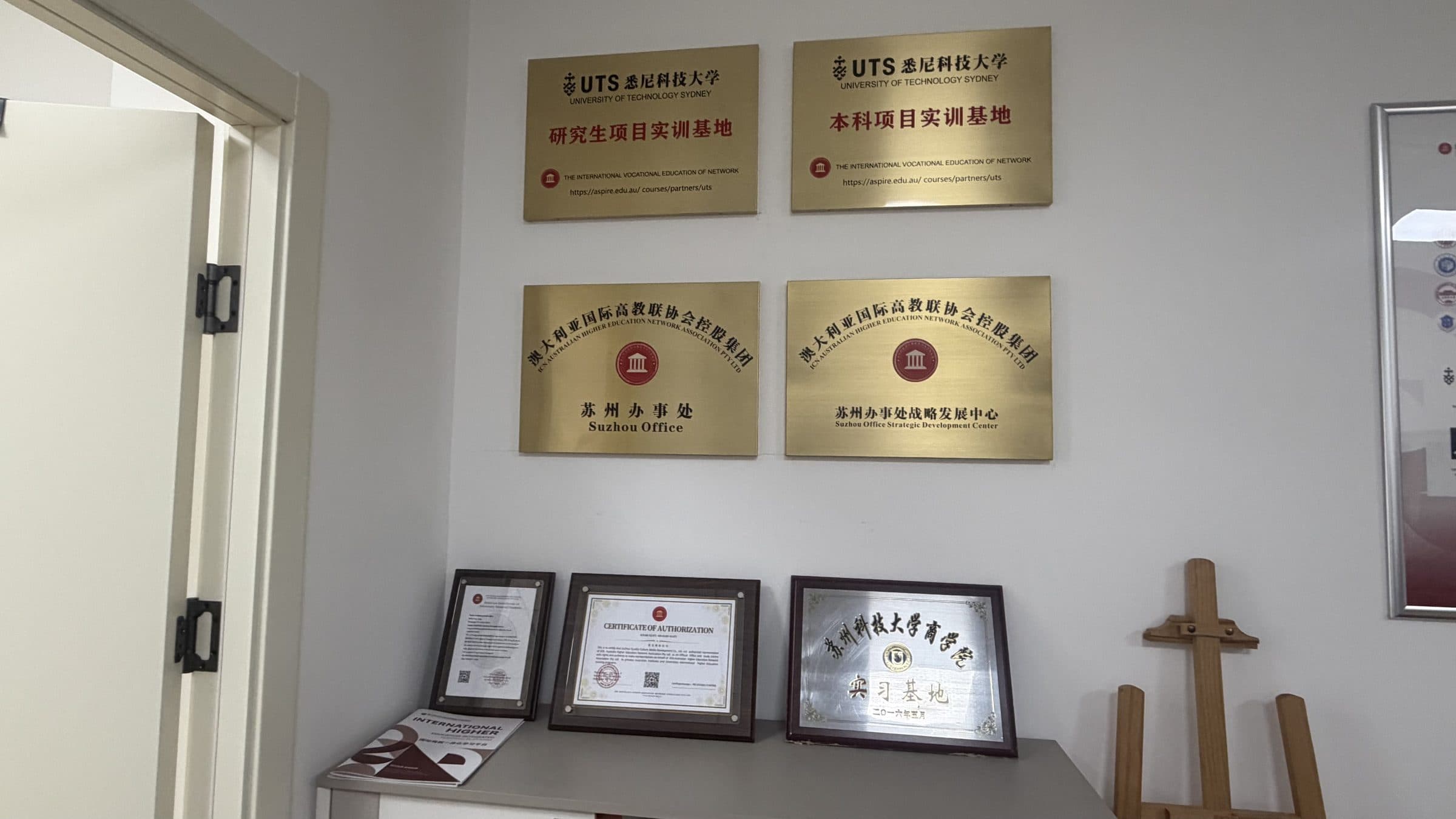Wall of accreditation plaques including UTS and ICN Suzhou office certifications